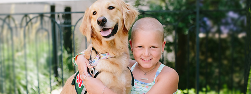 Sadie and Blair, a pet therapy dog, hugging in the butterfly garden at Children's Medical Center.