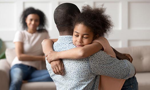 Dad hugging daughter while mom is watching and smiling.